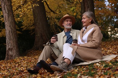 Photo of Affectionate senior couple with cups of coffee on blanket in autumn park
