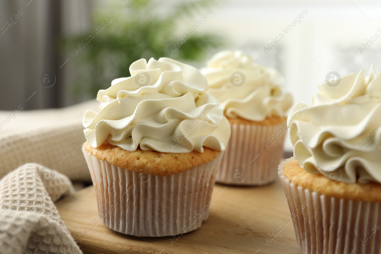 Photo of Tasty cupcakes with vanilla cream on wooden board, closeup