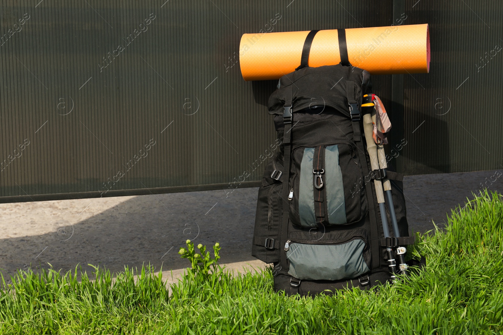 Photo of Backpack with trekking poles and camping mat on green grass. Space for text