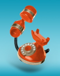 Image of Vintage orange corded telephone flying in air on light blue background