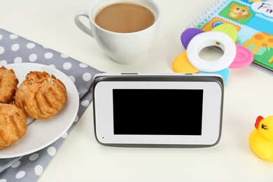 Photo of Modern monitor, cup of coffee, cookies and baby accessories on table, space for text. CCTV equipment
