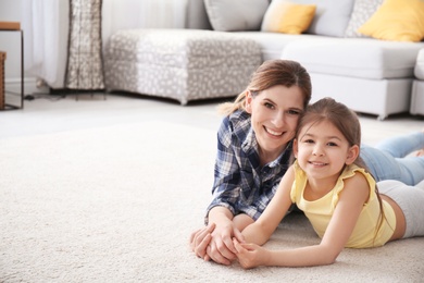 Photo of Cute little girl and her mother lying on cozy carpet at home