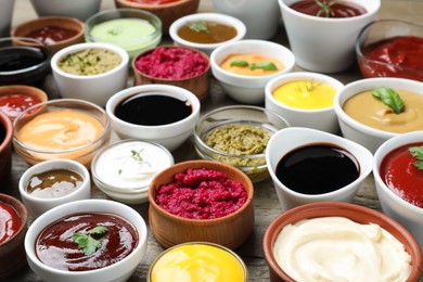 Photo of Many bowls with different sauces and herbs on wooden table