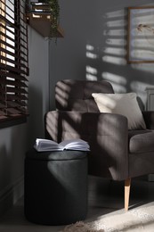 Stylish dark grey pouf and armchair in room. Home design