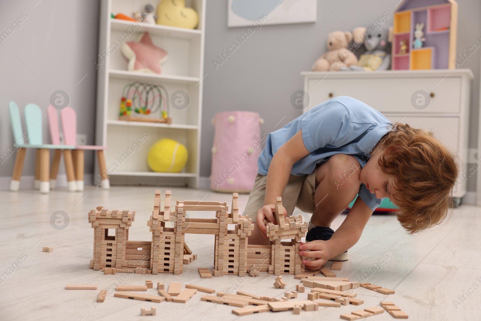 Photo of Little boy playing with wooden construction set on floor in room, space for text. Child's toy