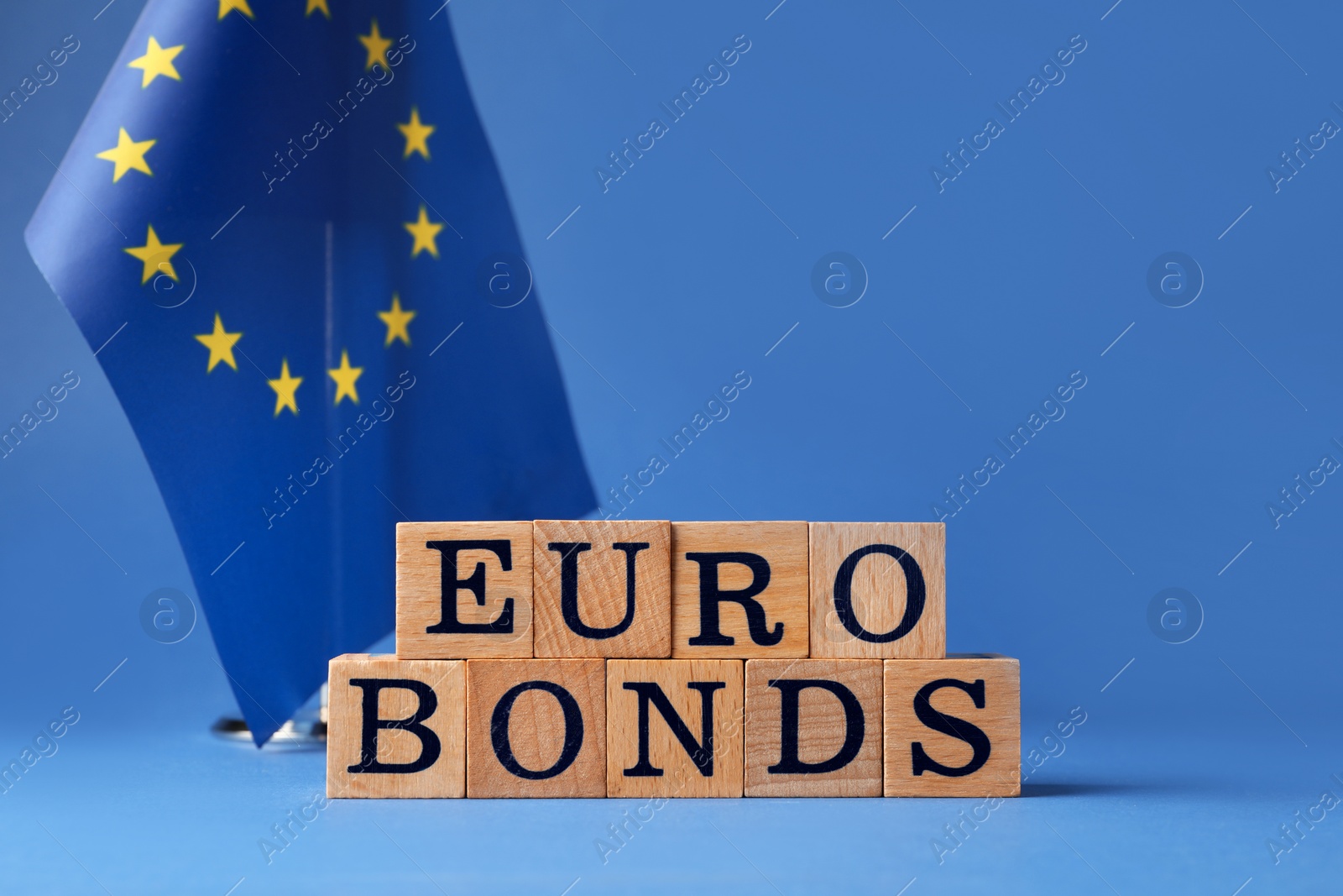 Photo of Word Eurobonds made of wooden cubes with letters and European Union flag on blue background