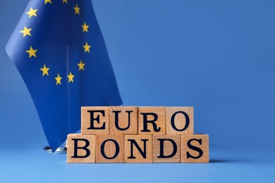 Word Eurobonds made of wooden cubes with letters and European Union flag on blue background