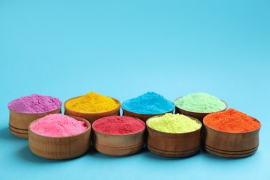 Photo of Colorful powders in bowls on light blue background, space for text. Holi festival celebration