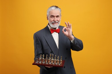Man with chessboard and game pieces showing OK gesture on orange background
