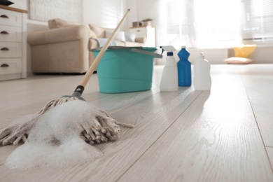 Photo of Bucket and different cleaning products indoors, focus on mop with foam