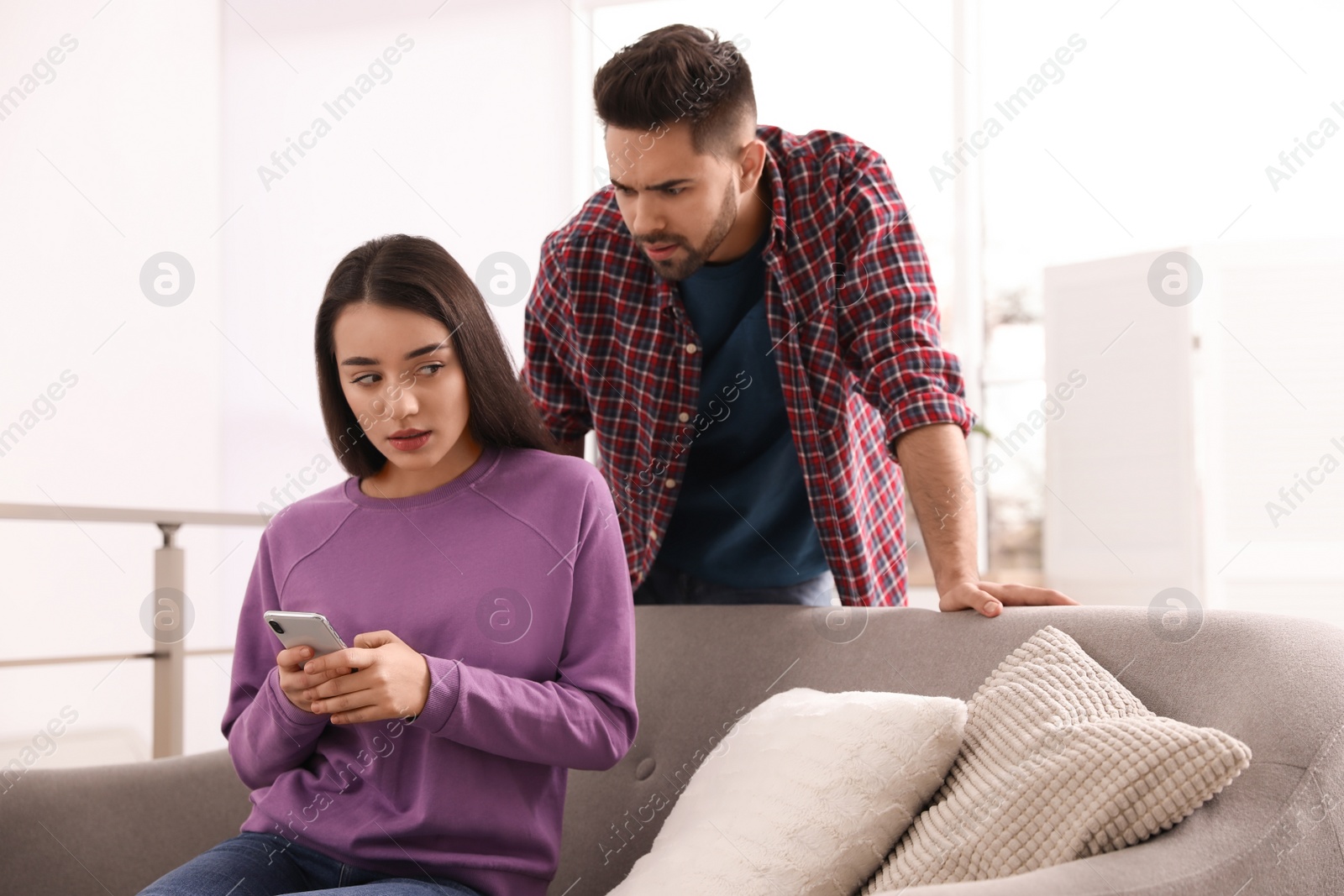 Photo of Distrustful young man peering into girlfriend's smartphone at home