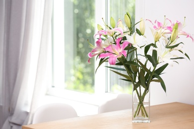 Photo of Vase with bouquet of beautiful lilies on wooden table indoors. Space for text