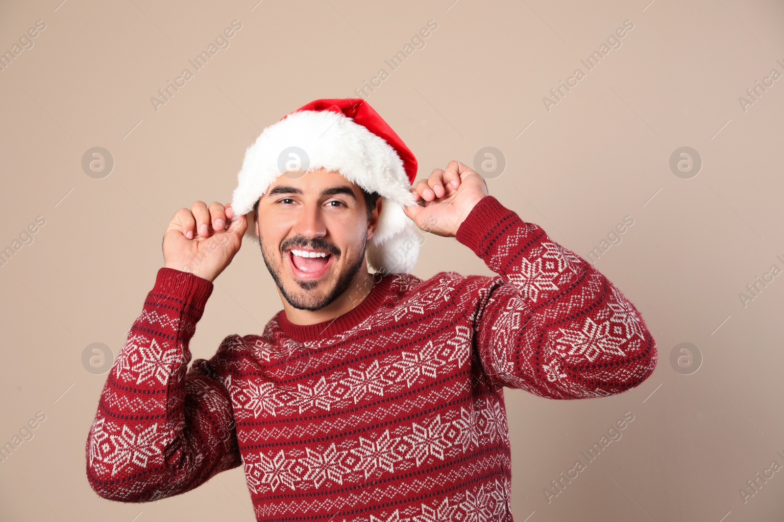 Photo of Portrait of young man in Christmas sweater and Santa hat on beige background