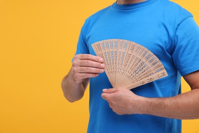 Man holding hand fan on orange background, closeup. Space for text