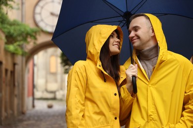 Lovely young couple with umbrella walking under rain on city street