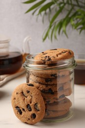 Photo of Glass jar with delicious chocolate chip cookies and tea on white marble table