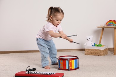 Photo of Cute little girl playing with drum, drumsticks and toy piano at home