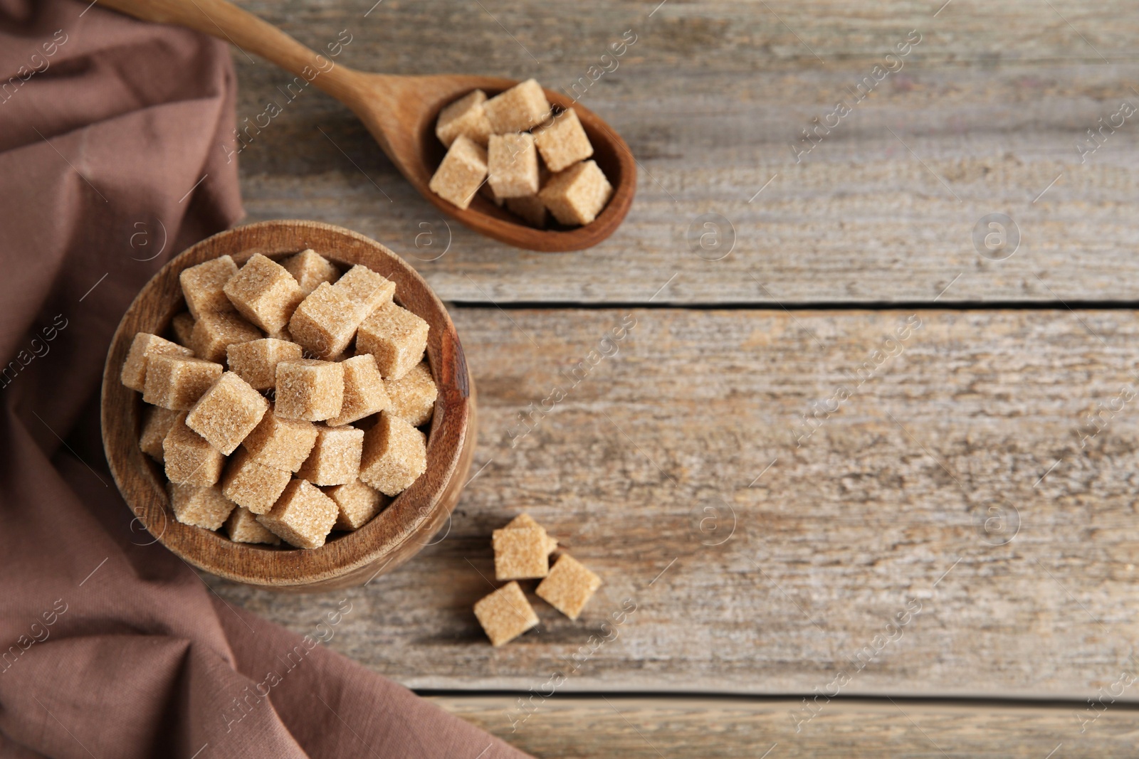 Photo of Bowl and spoon with brown sugar cubes on wooden table, flat lay. Space for text