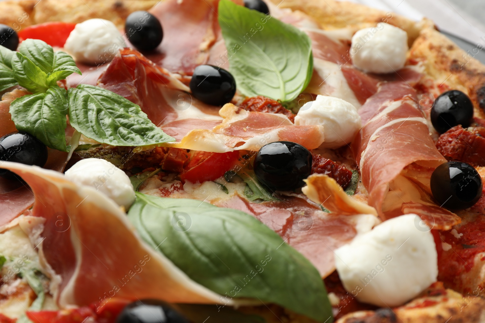 Photo of Tasty pizza with cured ham, olives, mozzarella cheese, sun-dried tomato and basil, closeup