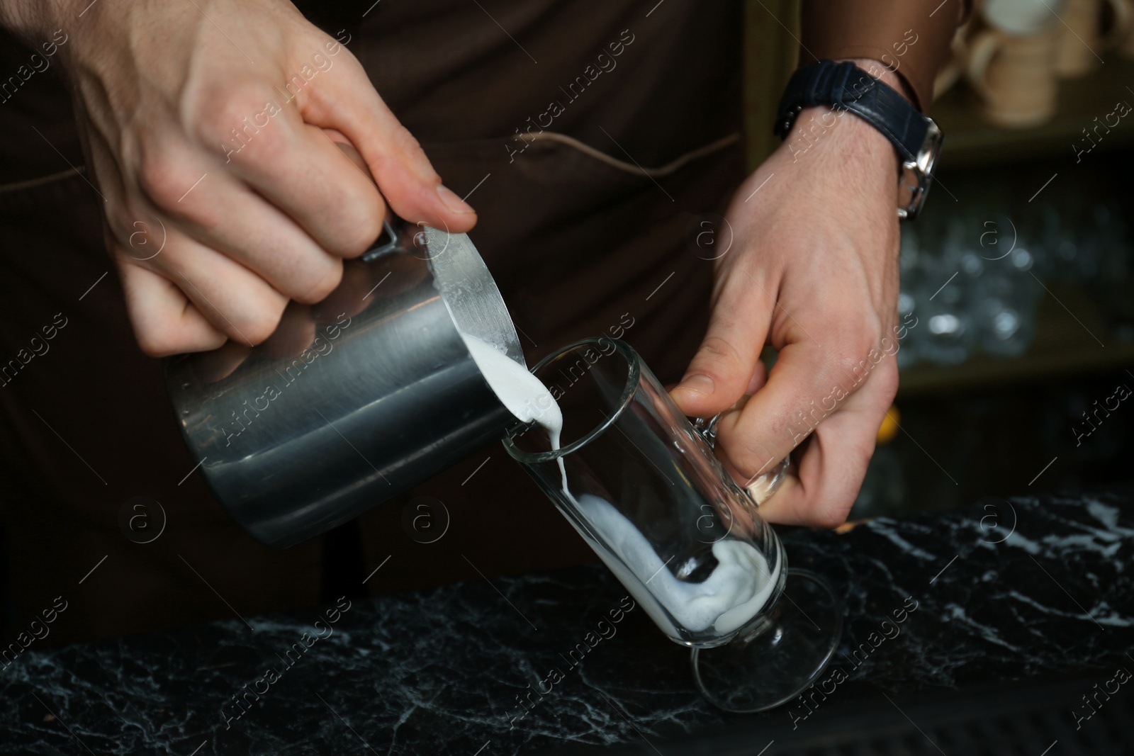 Photo of Barista pouring milk into glass cup for coffee drink at table