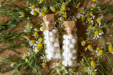 Photo of Bottles of homeopathic remedy and chamomile flowers on wooden background, flat lay