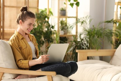Photo of Happy young woman with laptop on armchair at home