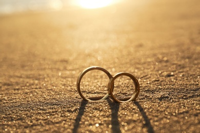 Photo of Gold wedding rings on sandy beach at sunset, closeup