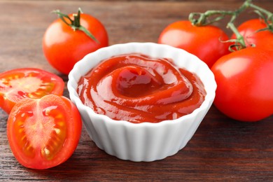 Bowl of tasty ketchup and tomatoes on wooden table, closeup