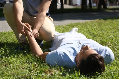 Photo of Passerby checking pulse of unconscious man outdoors. First aid