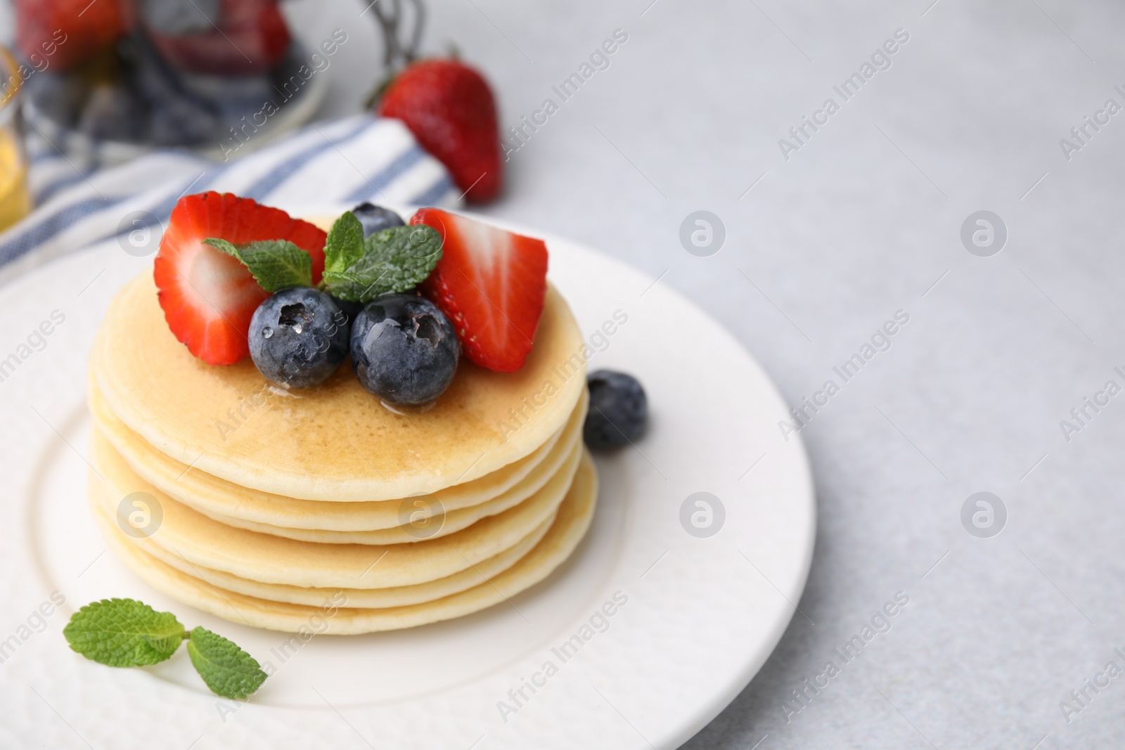 Photo of Delicious pancakes with strawberries, blueberries and honey on light grey table, closeup. Space for text