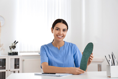 Photo of Young female orthopedist showing insole in clinic