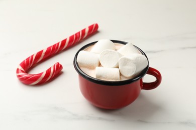 Photo of Tasty hot chocolate with marshmallows and candy cane on white marble table, closeup