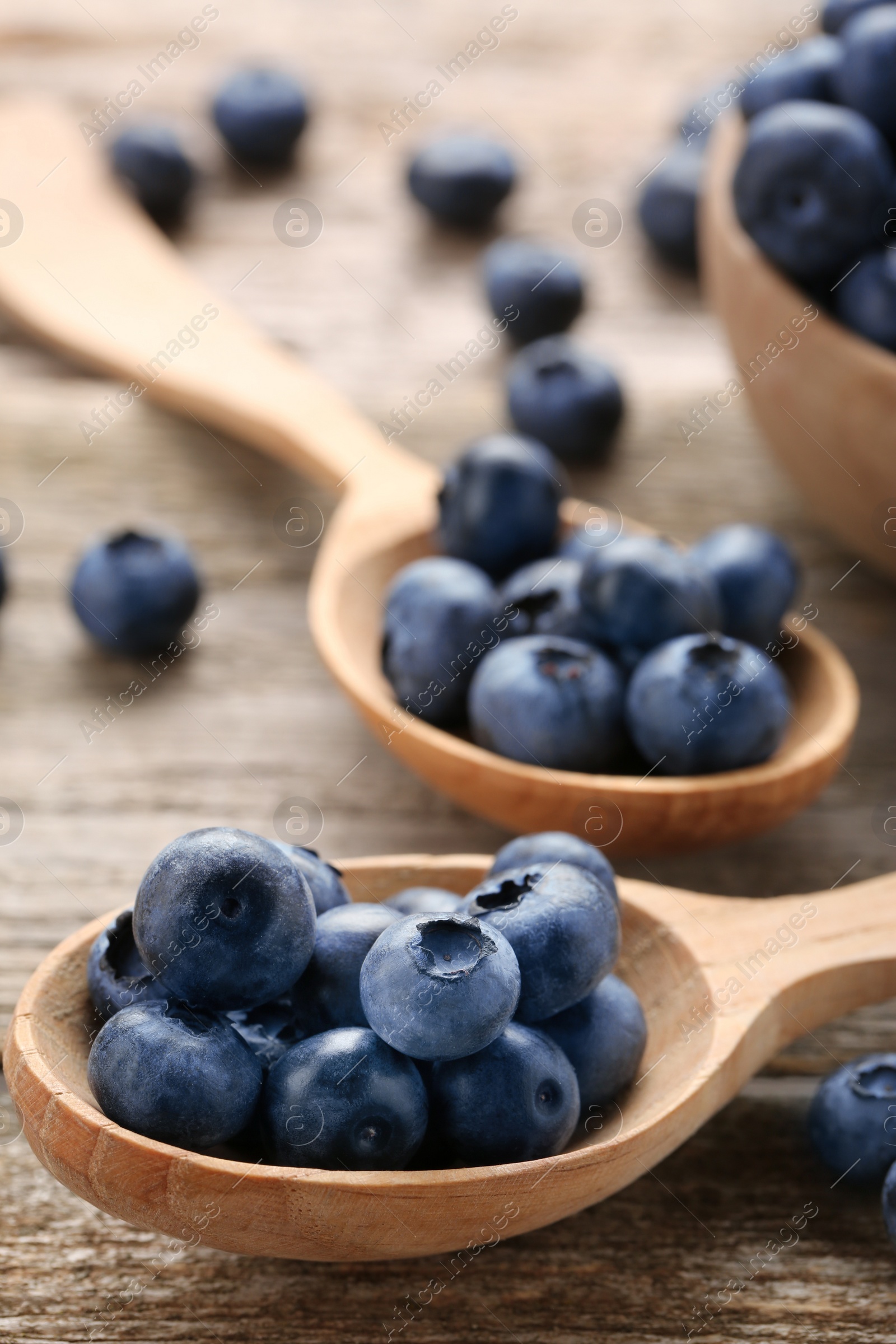 Photo of Spoons with tasty fresh blueberries on wooden table, closeup
