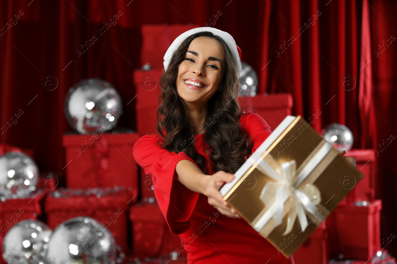 Photo of Beautiful woman in Christmas costume with gift near pile of presents indoors