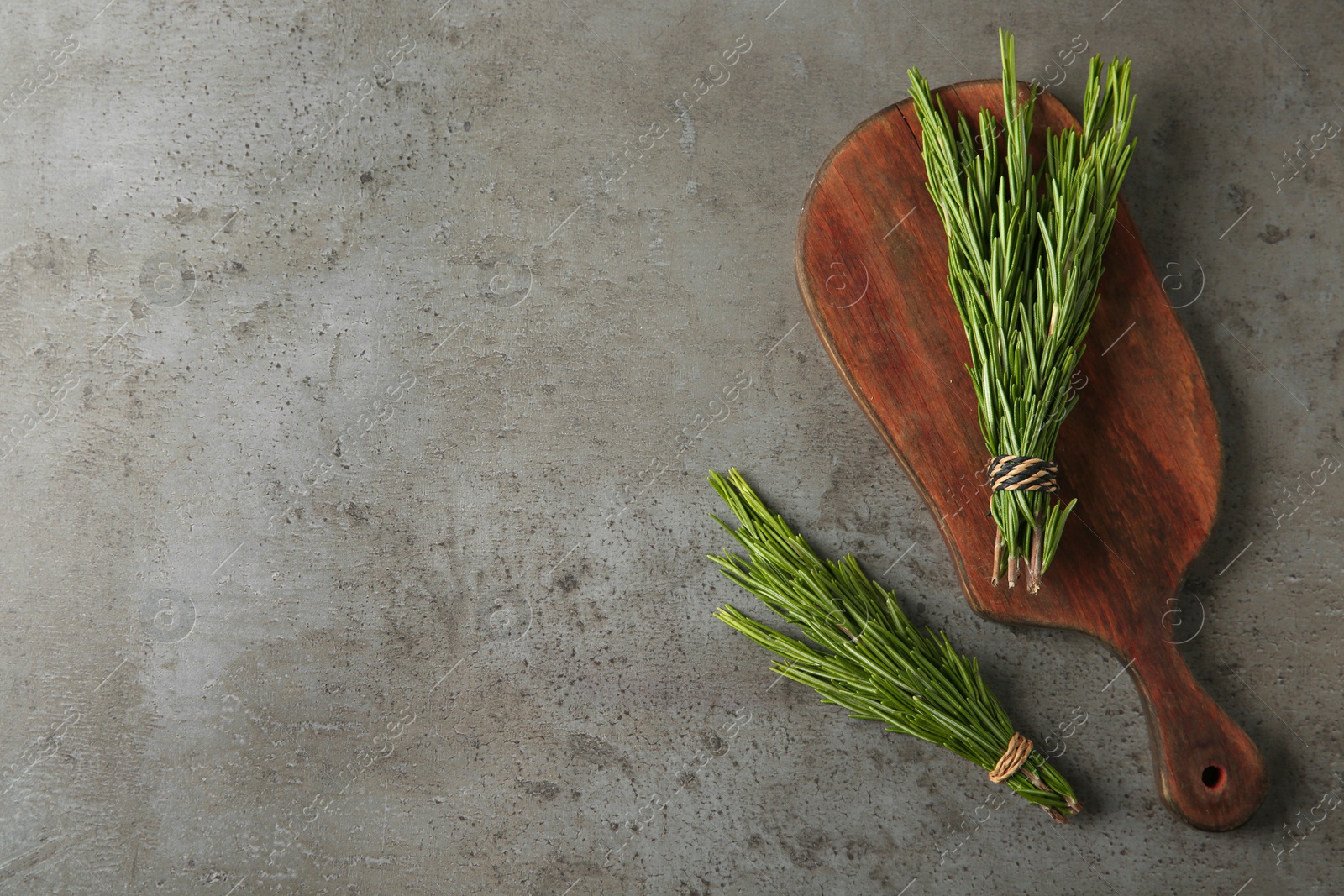 Photo of Board with bundles of fresh rosemary twigs on grey background, top view. Space for text