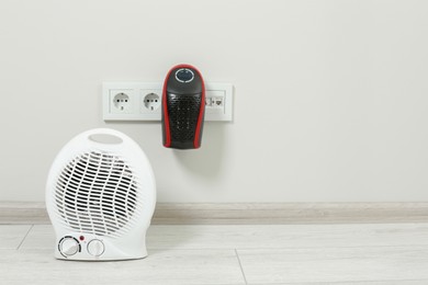 Modern electric compact and fan heaters indoors, space for text