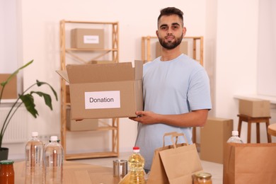 Volunteer with donation box and food products on table in warehouse