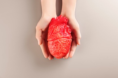 Woman holding model of heart on gray background. Heart attack concept