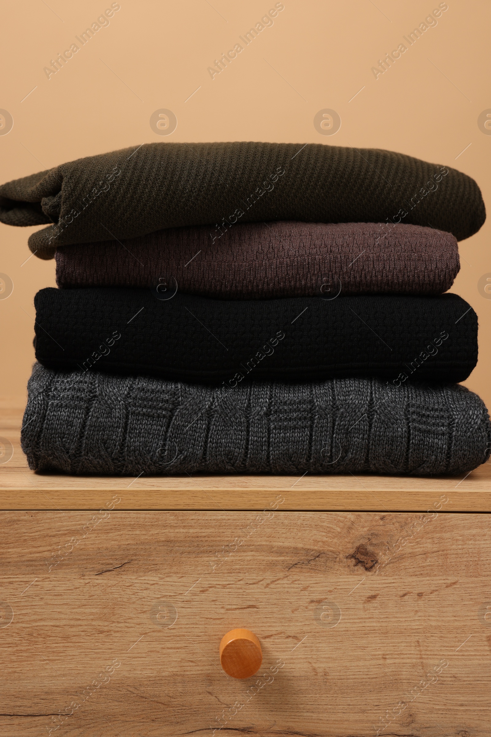 Photo of Different casual sweaters on chest of drawers against light brown background