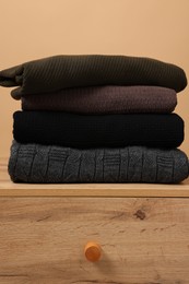 Photo of Different casual sweaters on chest of drawers against light brown background