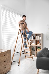 Photo of Smiling man on wooden folding ladder at home