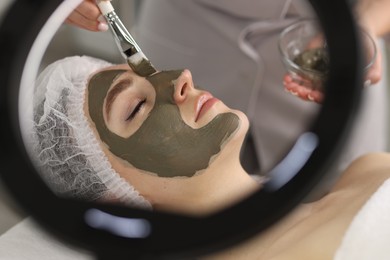 Photo of Cosmetologist applying mask on woman's face, closeup