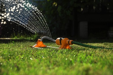 Photo of Automatic sprinkler watering green grass on sunny day outdoors. Irrigation system