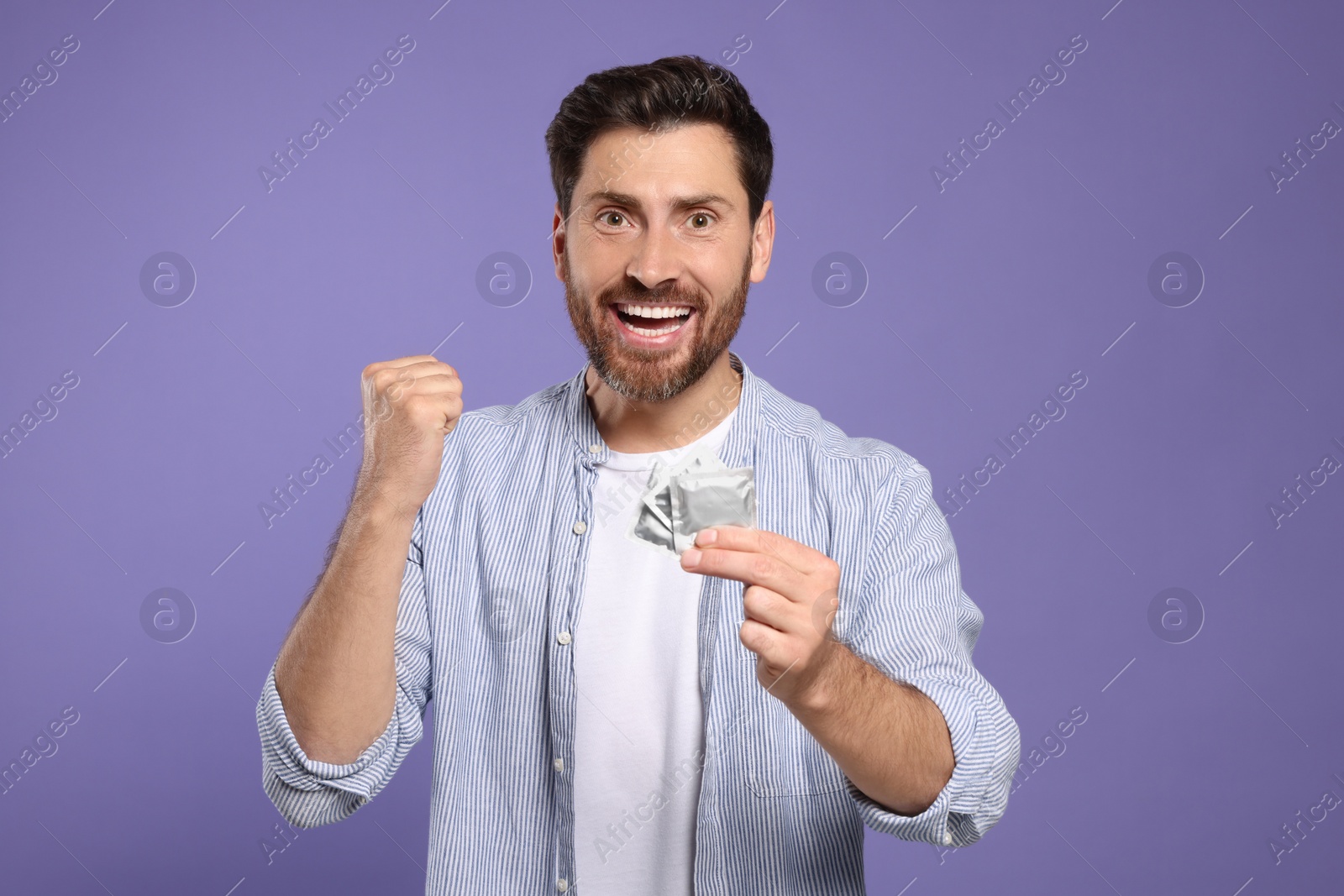 Photo of Emotional man holding condoms on purple background. Safe sex