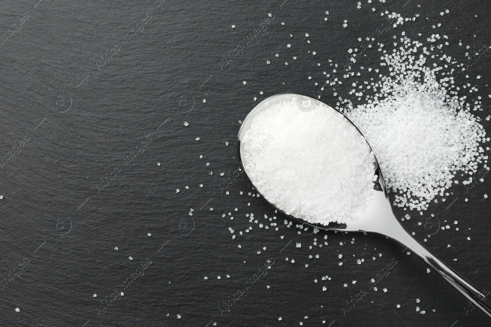 Photo of Granulated sugar and spoon on black table, top view. Space for text