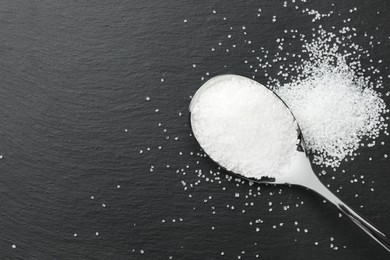 Granulated sugar and spoon on black table, top view. Space for text