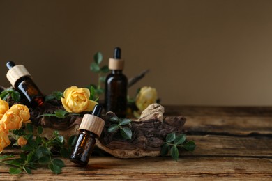 Bottles of rose essential oil and flowers on wooden table. Space for text