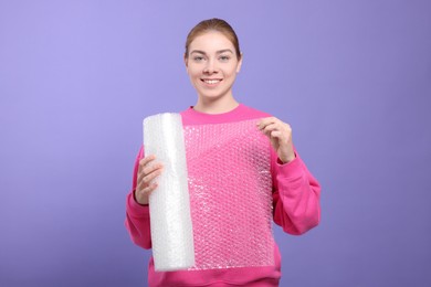 Photo of Woman holding roll of bubble wrap on purple background. Stress relief
