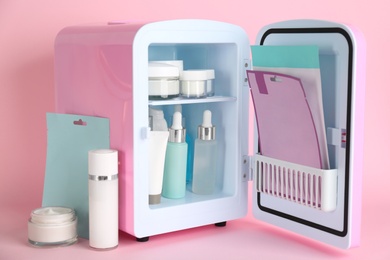 Open cosmetic refrigerator and skin care products on pink background