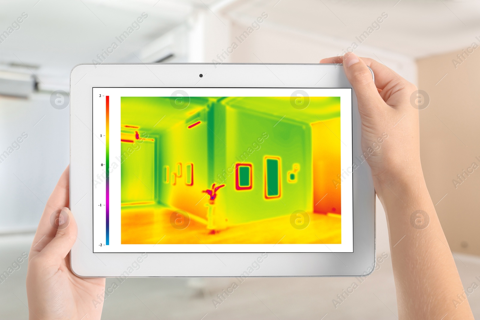 Image of Woman detecting heat loss in room using thermal viewer on tablet. Energy efficiency